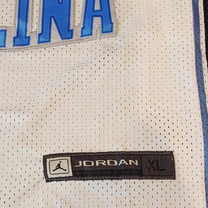 May include: White mesh jersey with blue accents and the word "INA" in blue. Features a "JORDAN" label with the size "XL". The jersey has a perforated design.