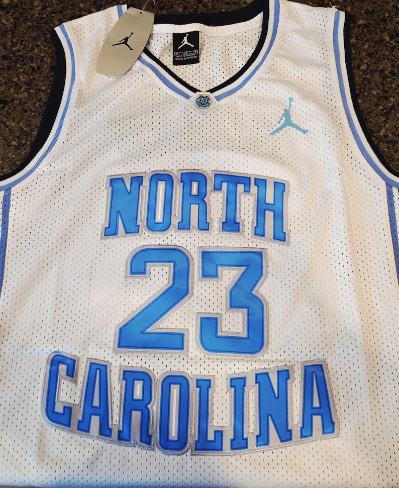 May include: White mesh basketball jersey with blue accents. Features the words "NORTH CAROLINA" and the number "23" in blue. Includes a tag with the Jordan logo.