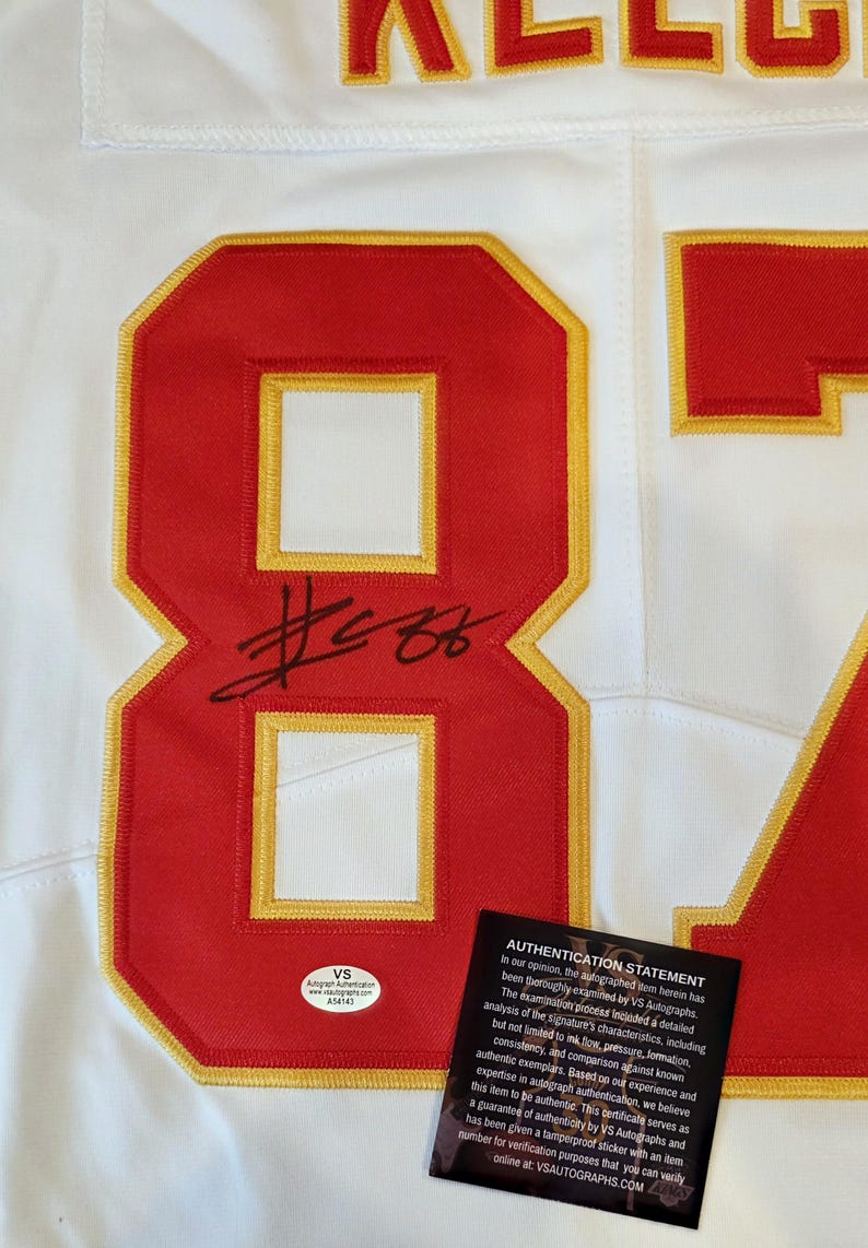 May include: White jersey with red and gold accents. Features the number 87 in red with a gold outline, and a black signature. Includes an authentication sticker and statement.