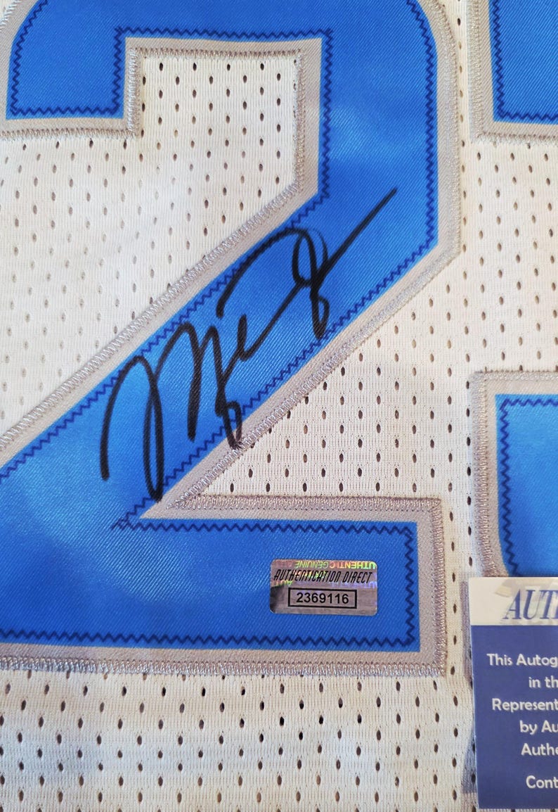 May include: Close-up of a white mesh jersey with blue accents and a black signature. The jersey has a blue number 2, a blue and silver trim, and a small authentication sticker.