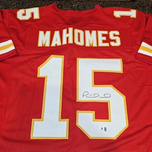 May include: A red football jersey with white and yellow accents. The jersey features the name "MAHOMES" across the chest and the number "15" on the front and back. The number "5" is on the shoulders.