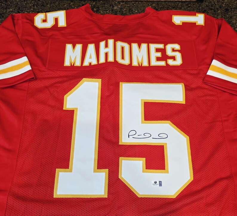 May include: A red football jersey with white and yellow accents. The jersey features the name "MAHOMES" across the chest and the number "15" on the front and back. The number "5" is on the shoulders.