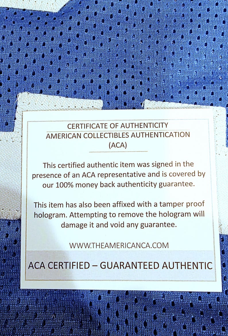 May include: A certificate of authenticity from American Collectibles Authentication (ACA) is displayed. The white card states the item is certified authentic, signed in the presence of an ACA representative, and covered by a money-back guarantee. The card also mentions a tamper-proof hologram.