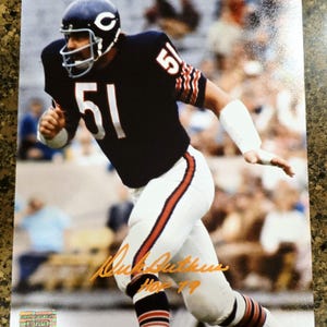 Puede incluir: Fotografía en color de un jugador de fútbol americano con una camiseta azul marino con el número 51 en blanco. El jugador lleva un casco azul marino con el logotipo "C" blanco. La firma del jugador está en tinta naranja, con "HOF 79" debajo.