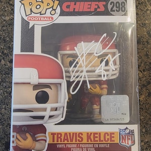 Puede incluir: Una figura de vinilo Funko Pop! de Travis Kelce con el uniforme de los Kansas City Chiefs, número 298. La figura está en una vitrina de plástico transparente, con el logo de la NFL y una firma.