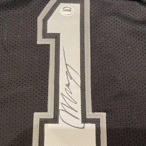 May include: Black jersey with a large, white and gray number 1 on the front. The number is outlined in gray and has a signature across it. An American Authentication sticker is visible.