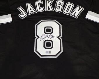 May include: Black jersey with the name "JACKSON" arched across the back in white lettering. Below, a large white number "8" is displayed, outlined in black, with a signature inside. The jersey has white and black trim on the sleeves.