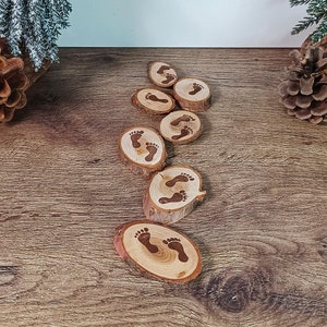 May include: A set of eight wooden slices with a footprint design, arranged in a line on a wooden surface. The slices are a light brown color and the footprints are a darker brown color.