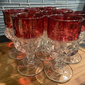May include: Set of six clear glass stemmed wine glasses with a ruby red rim. The glasses have a textured, diamond-like pattern.