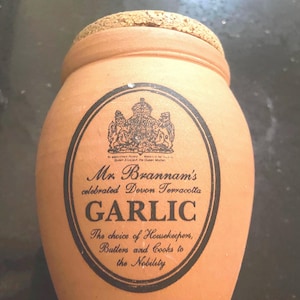 May include: A terracotta jar with a cork lid and a black and white label that reads "Mr. Brannam's celebrated Devon Terracotta GARLIC The choice of Housekeepers, Butlers and Cooks to the Nobility."