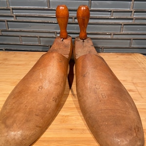 May include: Pair of vintage wooden shoe forms with wooden handles. The shoe forms are a light brown colour and appear to be well-worn. The handles are a darker brown. The number 8 is visible on one of the forms.