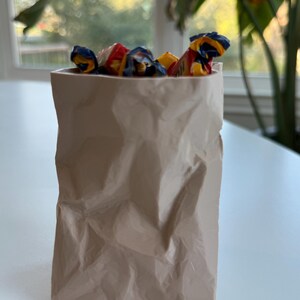 Może przedstawiać: Brązowa papierowa torba wypełniona kolorowymi, owiniętymi cukierkami.