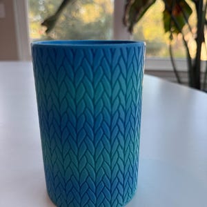 May include: A blue and green ombre ceramic cup with a knitted pattern.
