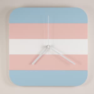 May include: Square wall clock with rounded corners, featuring horizontal stripes in light blue, pink, and white. The clock hands are white, and the clock face has a minimalist design. This clock is a decorative item.