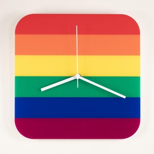 May include: A square wall clock with rounded corners, featuring a rainbow design with horizontal stripes in red, orange, yellow, green, blue, and purple. The clock has white hands and a white second hand.