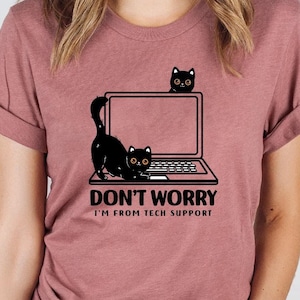 May include: A heather mauve t-shirt with a black cat peeking out from behind a laptop. The text on the shirt reads "Don't Worry I'm From Tech Support."