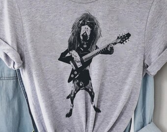 May include: A light gray t-shirt featuring a black and white illustration of a dog playing an electric guitar. The dog has long hair and is wearing a jacket. The shirt is knotted at the bottom.