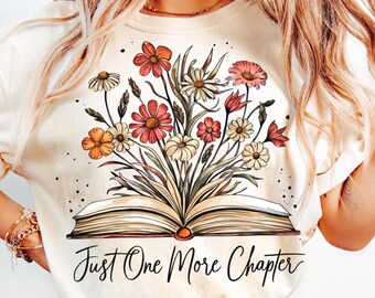 May include: A cream-colored t-shirt with a graphic of an open book with flowers growing out of it. The text "Just One More Chapter" is printed below the book.