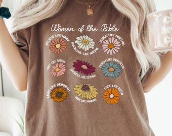 May include: An espresso-colored t-shirt featuring a graphic of nine colorful daisies arranged in a grid. Each flower is paired with text referencing biblical figures, including Believe Like Mary, Overcome Like Naomi, Serve Like Martha, and others.