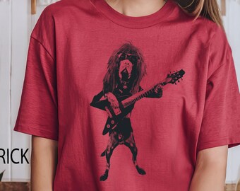 May include: A brick red short-sleeved t-shirt featuring a black graphic print of a dog with long hair wearing sunglasses and playing an electric guitar. The shirt has a crew neckline and a relaxed fit, showcasing a detailed illustration of the canine musician.