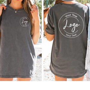 Puede incluir: Una camiseta de manga corta en color gris carb&oacute;n con un peque&ntilde;o logotipo circular en el pecho izquierdo y un logotipo circular grande a juego en la espalda. El dise&ntilde;o circular contiene el texto Your Text Logo Your Text en color blanco.