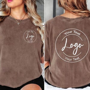 Puede incluir: Una camiseta marr&oacute;n de manga corta con un gr&aacute;fico circular blanco en el pecho izquierdo con el texto Your Text Logo. La parte posterior de la camiseta muestra una versi&oacute;n m&aacute;s grande del mismo gr&aacute;fico circular blanco con el texto Your Text Logo.
