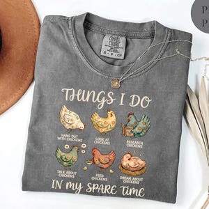 May include: A gray Comfort Colors t-shirt with the text "Things I Do" and illustrations of chickens. The shirt also says "Hang out with chickens", "Look at chickens", "Research chickens", "Talk about chickens", "Feed chickens", and "Dream about chickens" in my spare time.