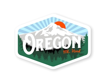 May include: A white sticker with a blue and white sky, a white mountain with an orange sun, green trees, and the text "Oregon Mt. Hood".