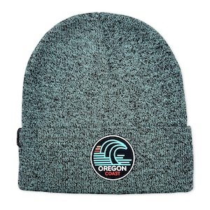May include: A teal and black knit beanie with a folded brim. The beanie features a circular patch with the words "Oregon Coast" and a wave design in blue, red, and white.