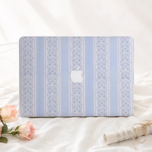 May include: A laptop cover featuring a repeating pattern of vertical light blue stripes alternating with white bands decorated with a delicate blue floral lace design. The center of the cover displays a cutout for a silver Apple logo.