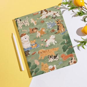 May include: A green notebook featuring a playful illustration of various dog breeds in a park setting. The cover design includes a white stylus and is set against a yellow and white background. The dogs are depicted in a cartoon style.