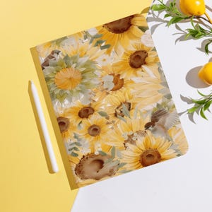May include: A tablet case featuring a vibrant floral design of yellow sunflowers and green leaves. The case has a watercolor effect with a bird illustration. A white stylus rests on a yellow surface.