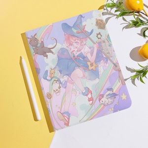 Pode incluir: Uma capa de tablet colorida com uma ilustração em estilo anime de uma bruxa, um gato e um arco-íris. O design inclui elementos caprichosos. Uma caneta branca está colocada ao lado.