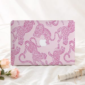 May include: A laptop skin featuring a repeating pattern of bright pink leopards on a light pink background. The design includes a central cutout for an Apple logo, showcasing the feline figures in various dynamic poses across the rectangular surface.