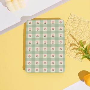 May include: A rectangular, rounded-corner notebook with a light green gingham pattern. Each square features a pink tulip. The notebook is on a yellow surface with other decorative elements.