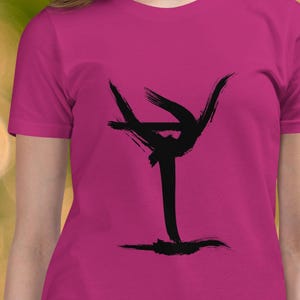 May include: A magenta t-shirt featuring a black abstract design resembling a cocktail glass. The shirt is short-sleeved and made of a soft material. The design is a bold, minimalist graphic.