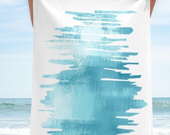 May include: White beach towel with a blue abstract watercolour design. The design features horizontal brushstrokes in varying shades of blue, creating a textured, artistic look. The towel is held up against a beach backdrop.