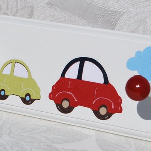 May include: White wooden wall hook with three colorful car decals and three round knobs. The cars are yellow and red, with black outlines. A blue cloud and a black star are also featured.