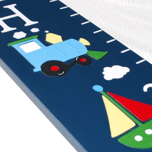 May include: A navy blue wooden growth chart with white markings and a colorful train and sailboat design. The chart measures up to 2 feet. The letter "H" is at the top.