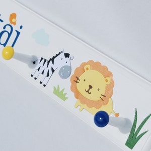 May include: White wooden wall hook with the name "Etai" in blue script, featuring a cartoon zebra, lion, and bird. Includes yellow and blue knobs for hanging items. Decorative and functional.