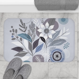 May include: A gray and white floral bath mat with a blue and gray abstract design. The mat features a large white flower with a gray center and gray leaves.