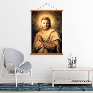 Może przedstawiać: Oprawiony portret mężczyzny z długimi włosami i aureolą, ubranego w kremową szatę. Grafika jest wyświetlana na drewnianej ramie do zawieszania. Tło ma ciepły, złoty odcień.