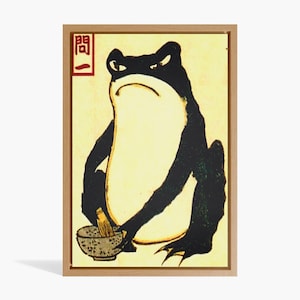 May include: A framed illustration of a black frog sitting on a yellow background. The frog is holding a wooden spoon and a bowl. The Japanese character "開" is written in red on the top left corner of the frame.
