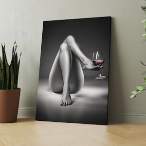 May include: Black and white canvas art print featuring a person's legs and torso, with a glass of red wine. The artwork is displayed on a wall next to a potted plant. The image has a grayscale color palette.