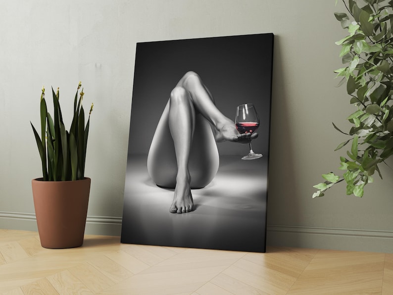 May include: Black and white canvas art print featuring a person's legs and torso, with a glass of red wine. The artwork is displayed on a wall next to a potted plant. The image has a grayscale color palette.