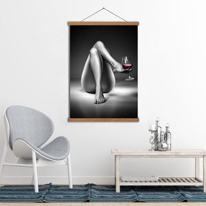 May include: Black and white wall art print featuring a person's legs and a glass of red wine. The artwork is displayed on a wooden frame, adding a touch of elegance to the room's decor. The image is a grayscale photograph.