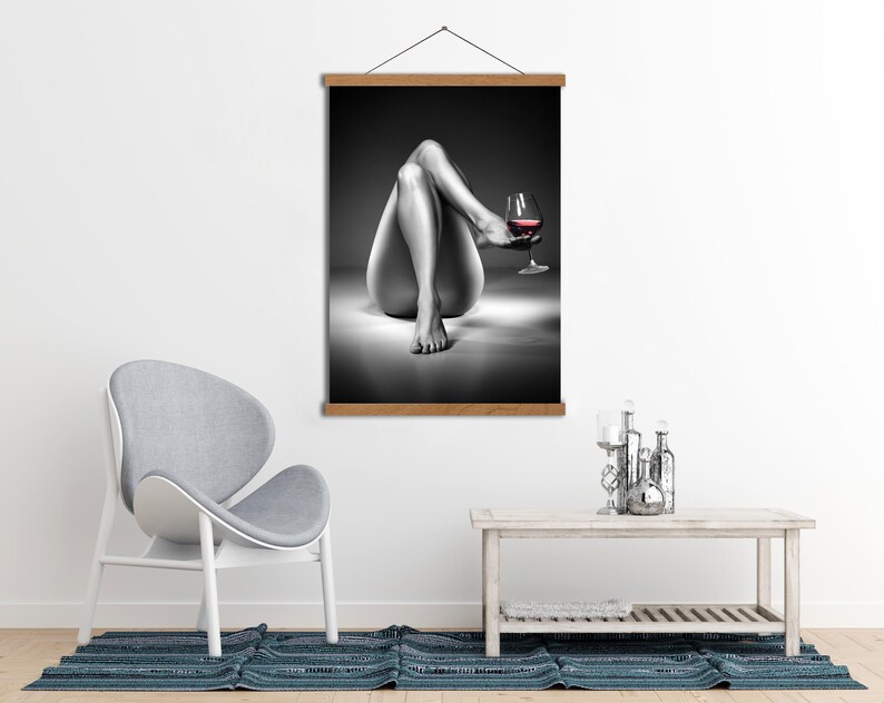 May include: Black and white wall art print featuring a person's legs and a glass of red wine. The artwork is displayed on a wooden frame, adding a touch of elegance to the room's decor. The image is a grayscale photograph.
