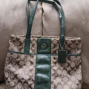 May include: A brown and green Coach tote bag with a signature pattern and a green snakeskin-like trim. The bag has two top handles and a zipper closure.