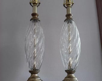 May include: A pair of clear glass table lamps with gold bases and twisted glass shades. The bases are square and have a wood-like finish.