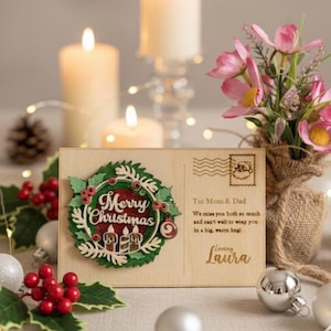 May include: A wooden Christmas postcard with a wreath design and the words "Merry Christmas." The postcard includes a message to Mom & Dad and is decorated with candles, ornaments, and flowers.